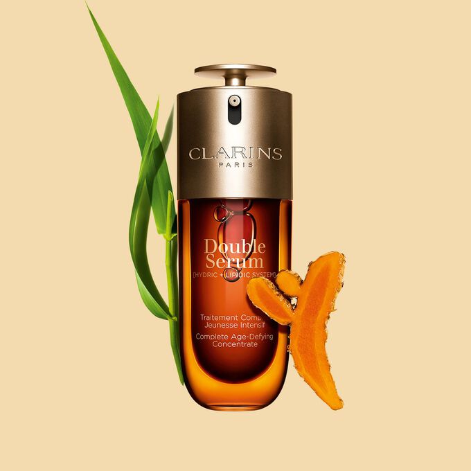 Packshot of the Clarins Double Serum displayed in front of its ingredient, including curcuma, on a gold background