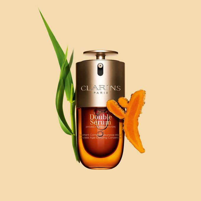 Packshot of the Clarins Double Serum displayed in front of its ingredient, including curcuma, on a gold background